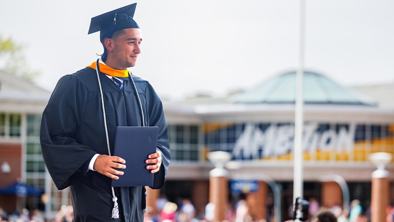 Graduate crosses stage with student center in the background