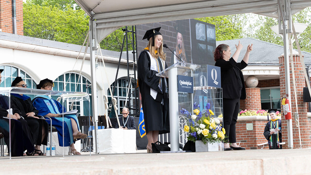 female student speakers stands at the podium in her cap and gown