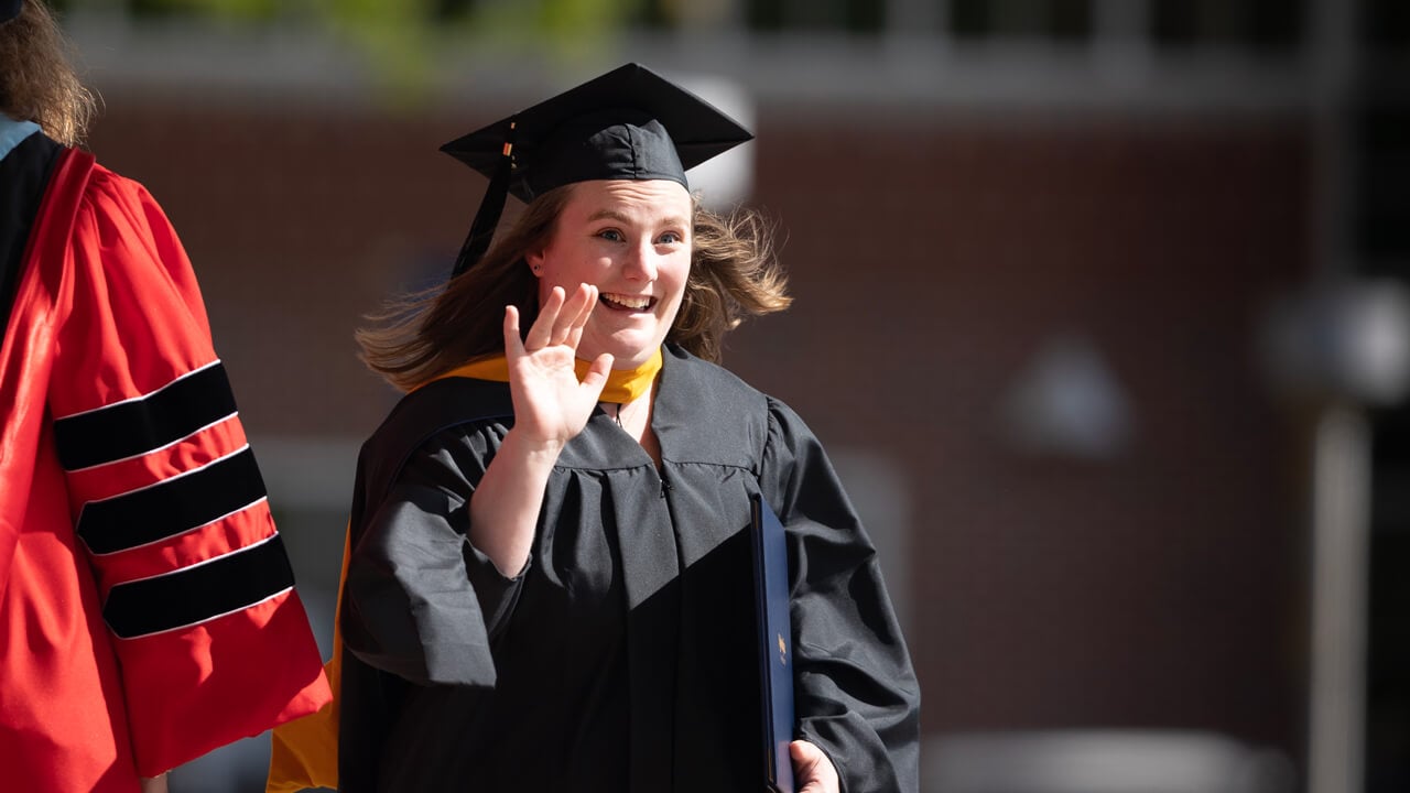 A graduate holds her diploma and waves excitedly