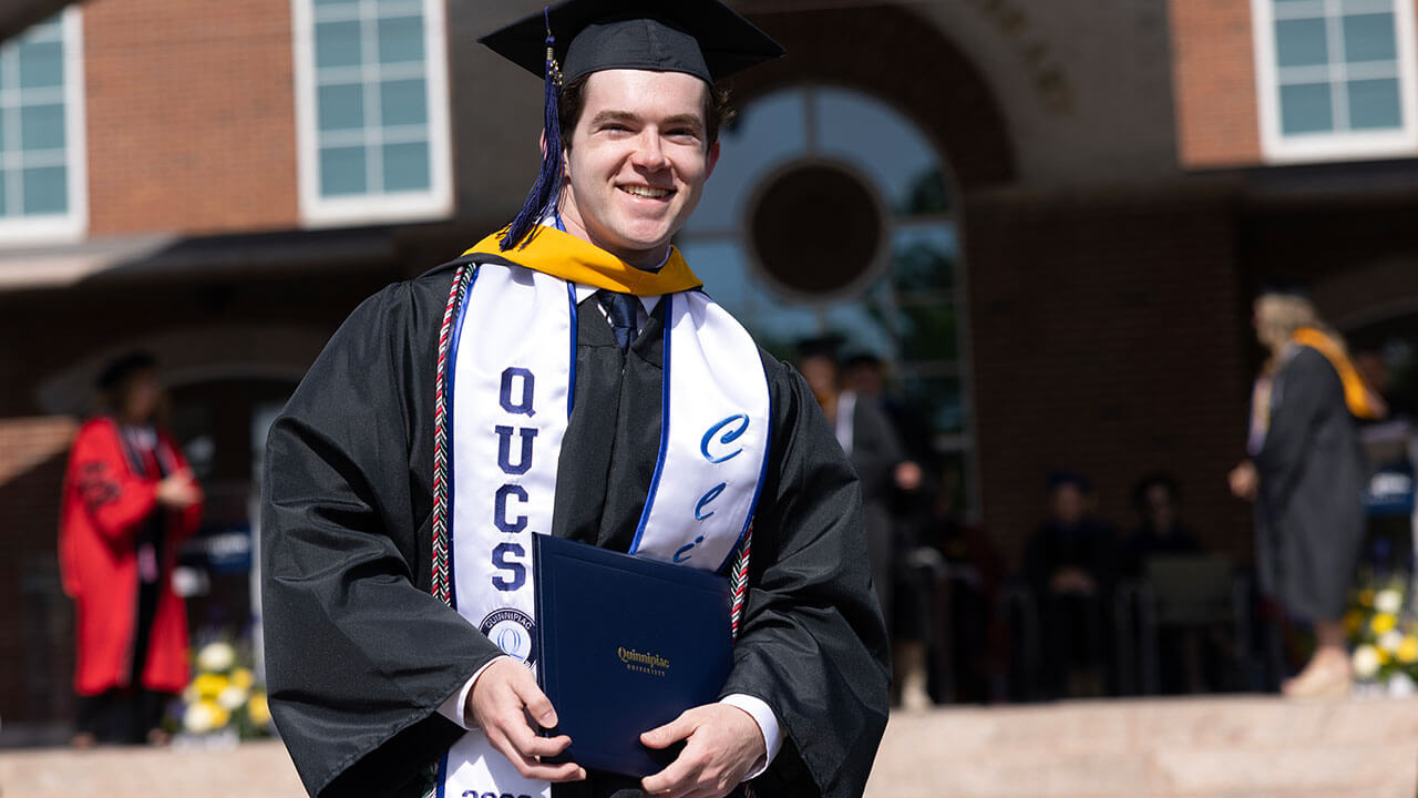 male graduate smiles while holding his diploma