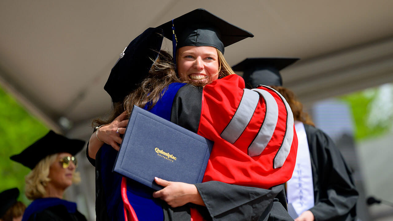 female graduate grins and hugs the dean of health sciences