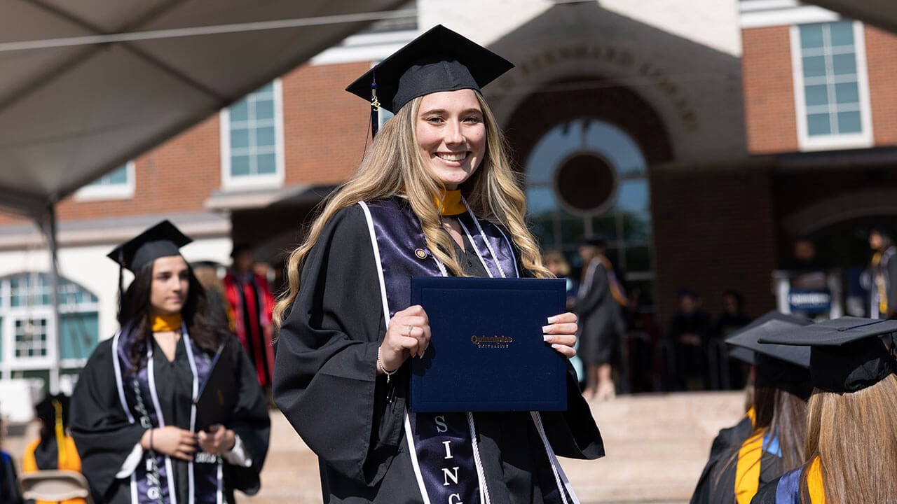 graduate poses with her diploma in the center aisle