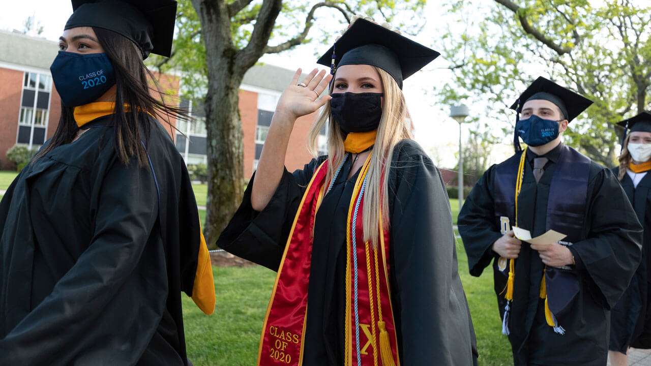 Graduate waving at camera walking on Quad
