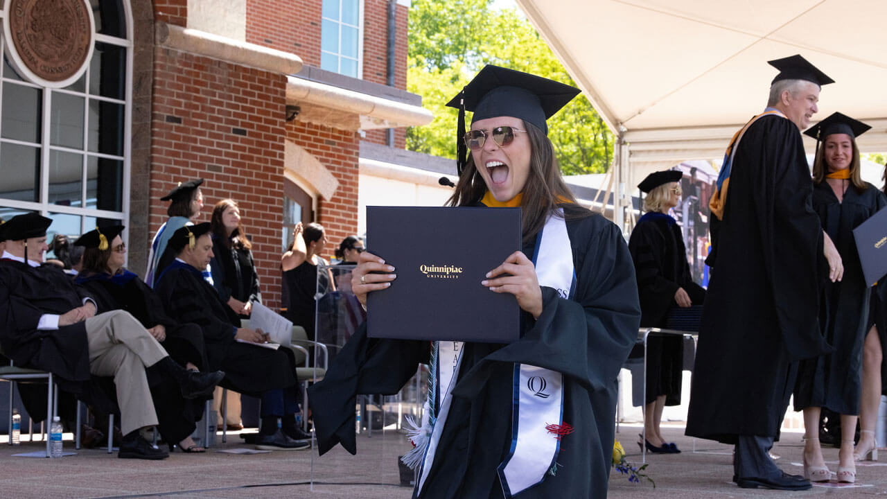Graduate holds her diploma and is cheerfully screaming in excitement