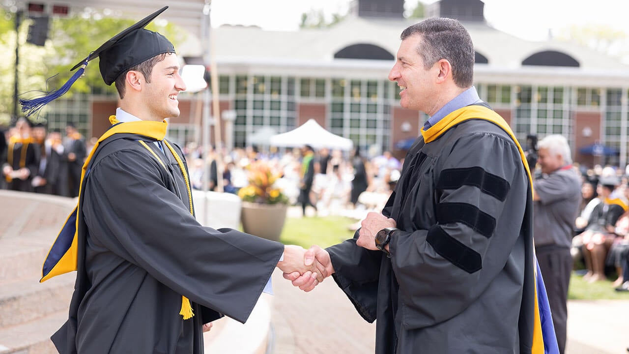 Student and professor shaking hands on the quad