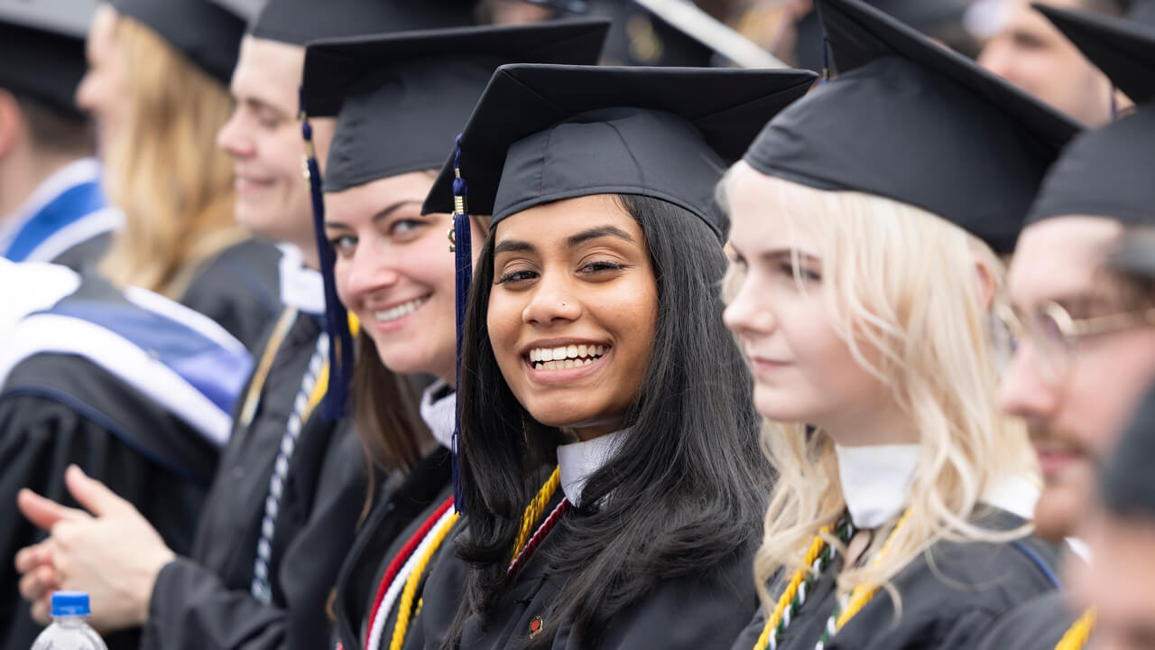 Graduates look around and smile while sitting at Commencement