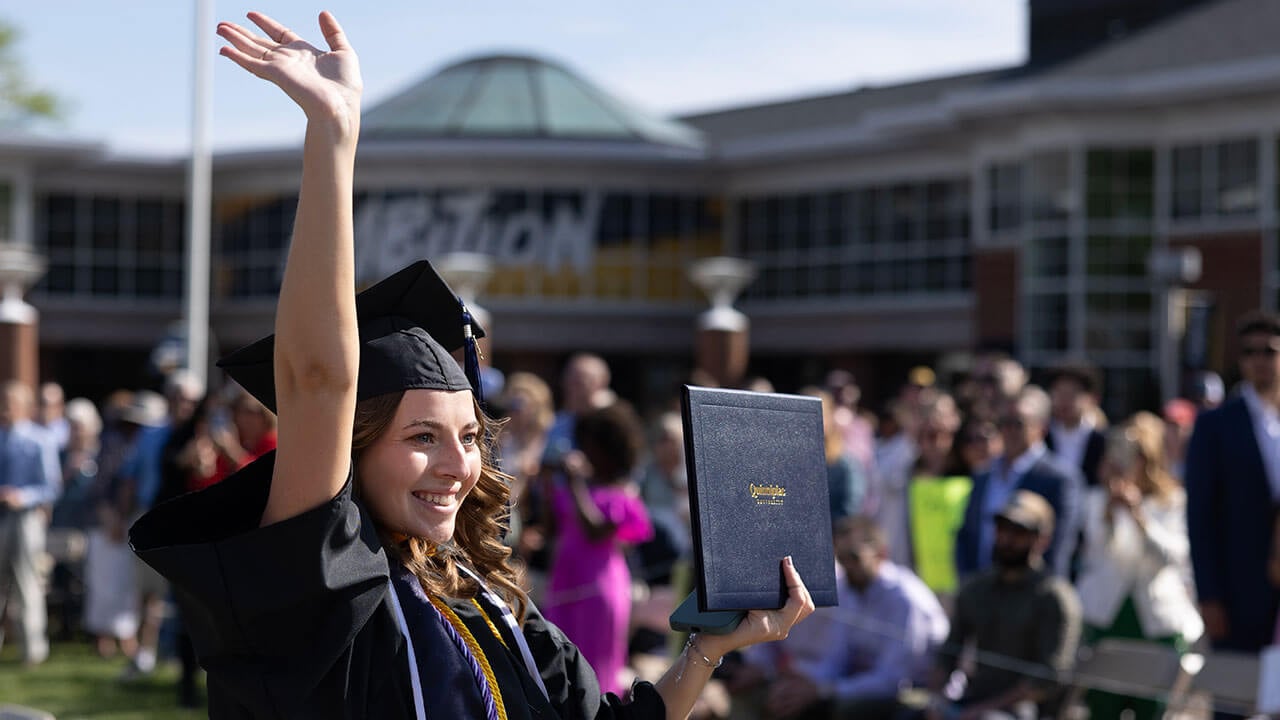 graduate holds up her diploma and waves to an audience member