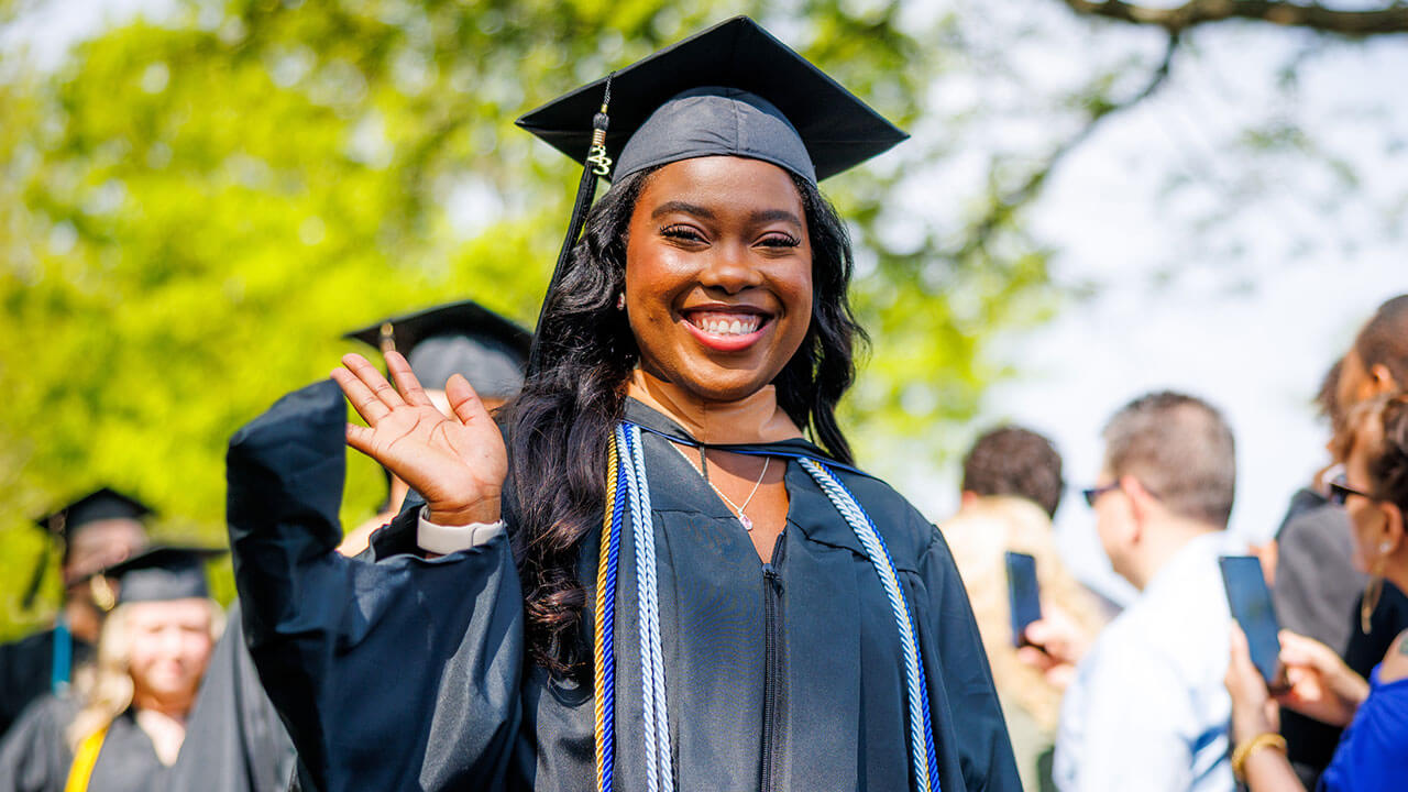 Business student waving to camera in her cap and gown
