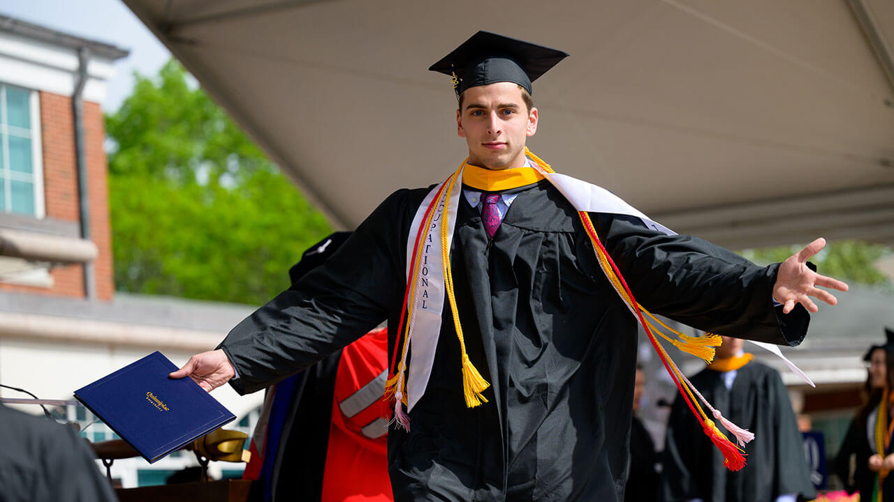 male graduate gestures with his arms out as he exits the stage
