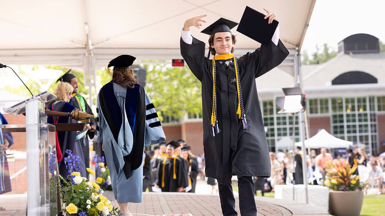 Student walking across the stage holding up peace signs with his diploma