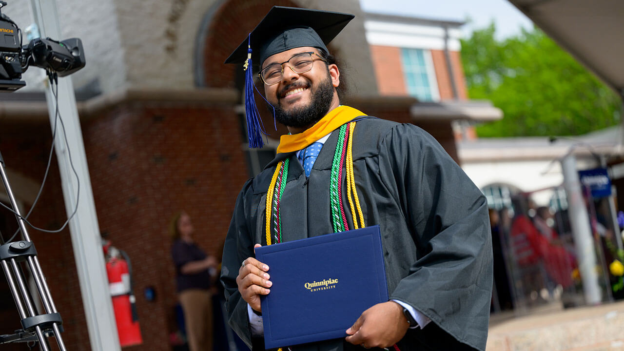 male graduate grins strongly while displaying his diploma for the camera