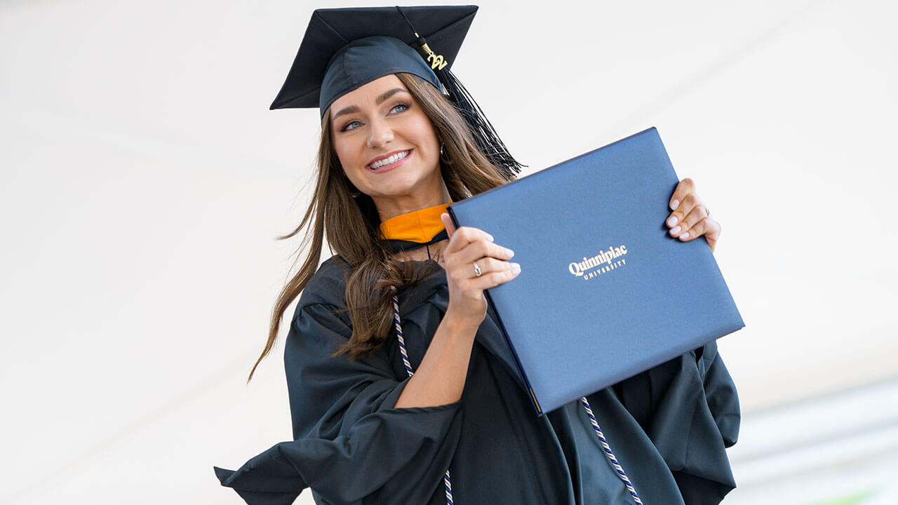 Graduate smiles off stage while holding up diploma