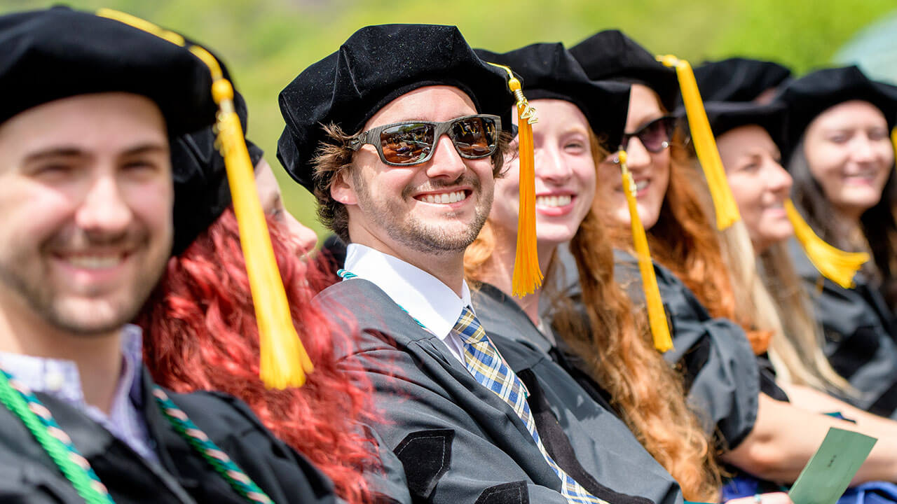 Graduates smile in their seats, with graduate in sunglasses in focus