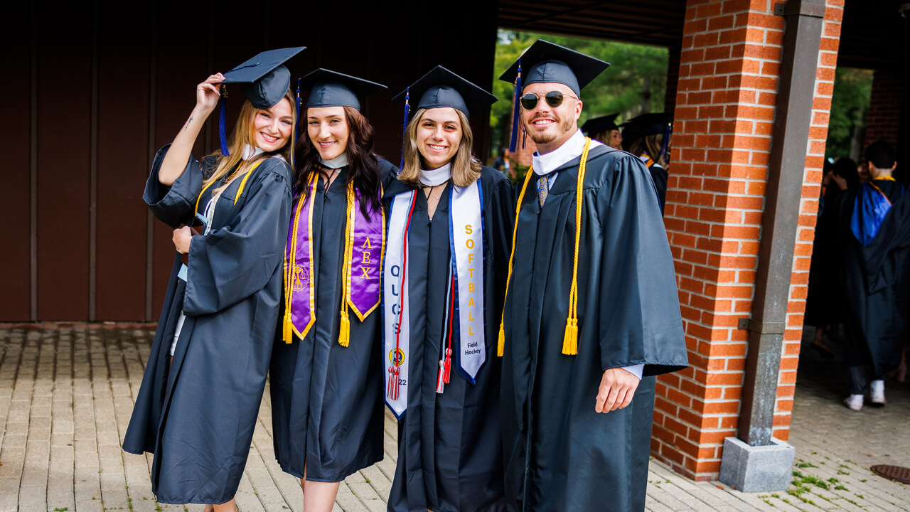 Four graduates pause for a photo in front of a brick building