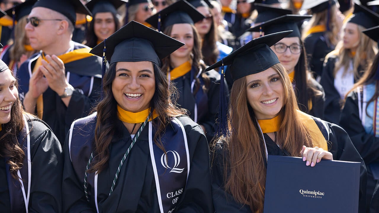 Rows of students smile and hold their diplomas during their commencement ceremony