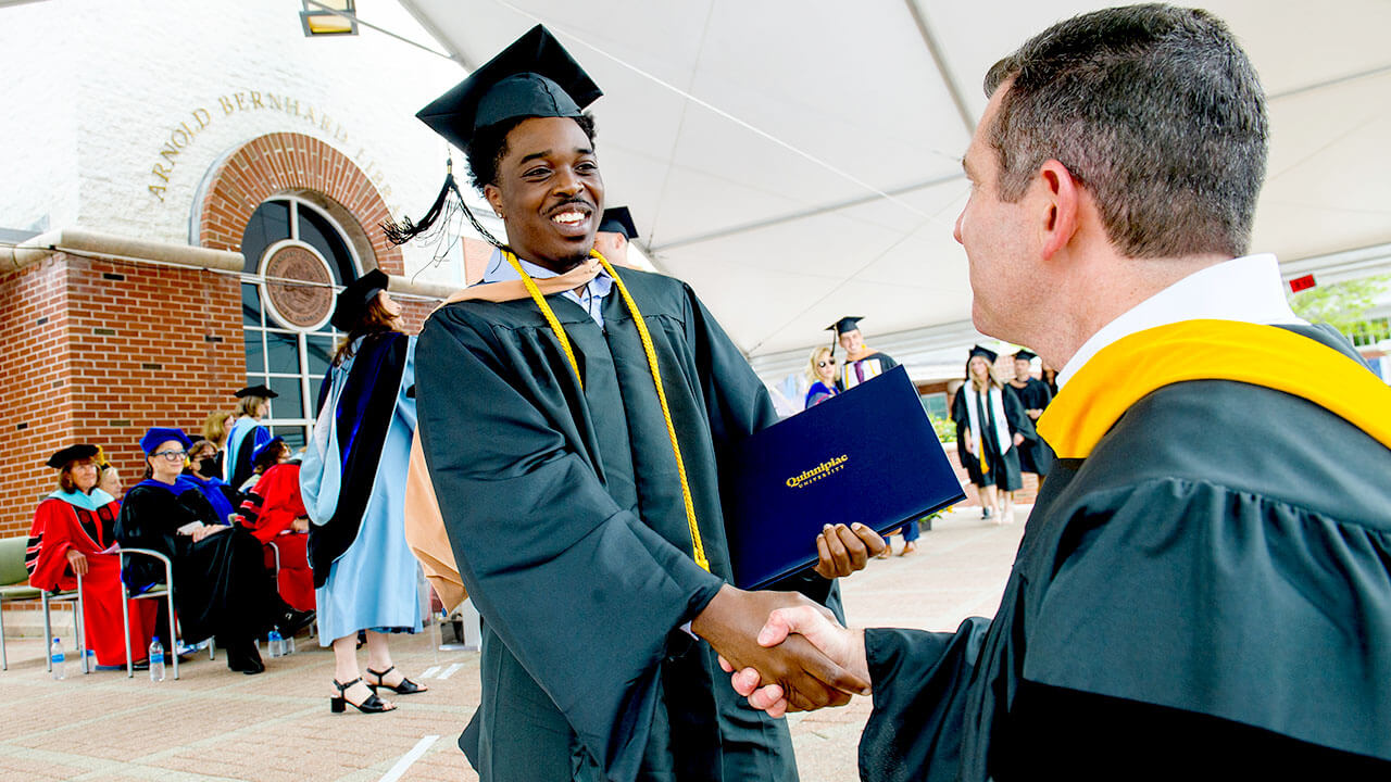 A graduate shakes hands with a faculty member on stage