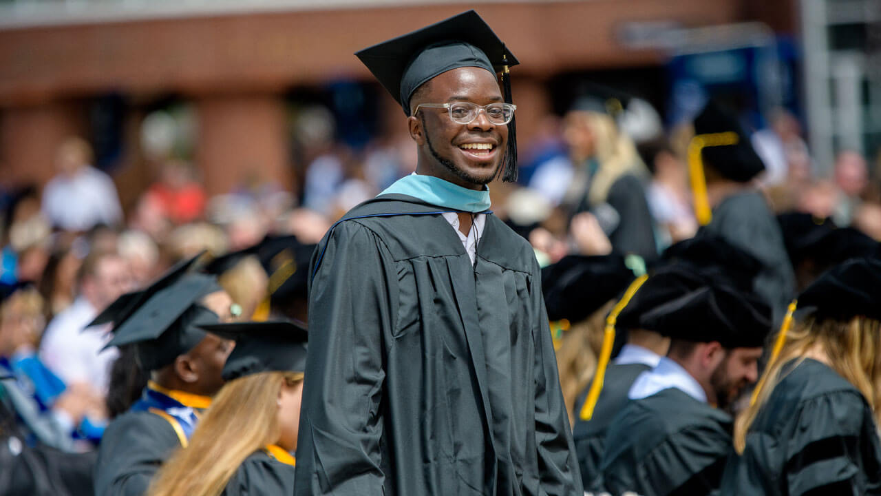 Graduating graduate student smiles and walks in the crowd