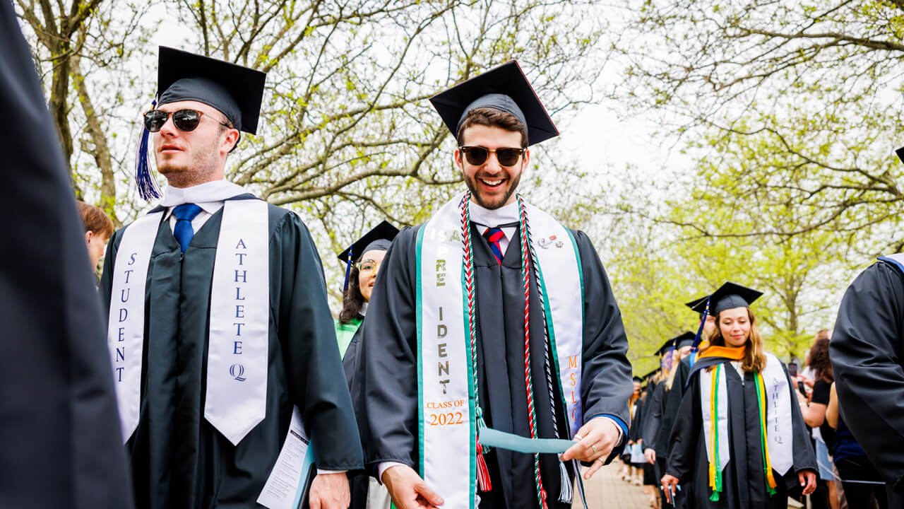 Two graduates smile as they walk across the quad