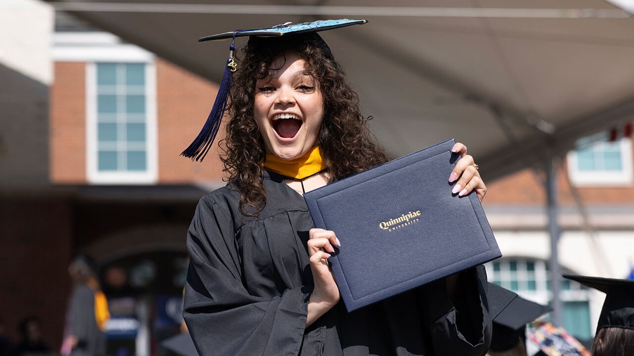graduate smiles widely while displaying her diploma