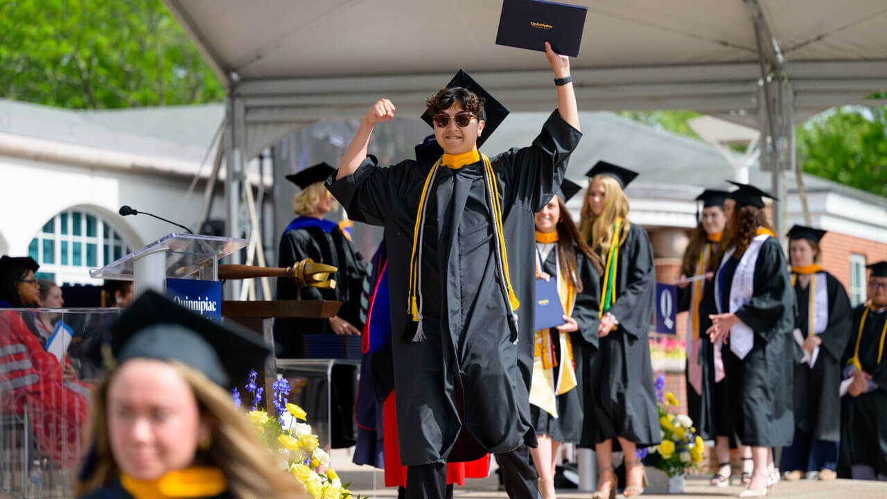 Graduate fist bumps the air and holds up diploma
