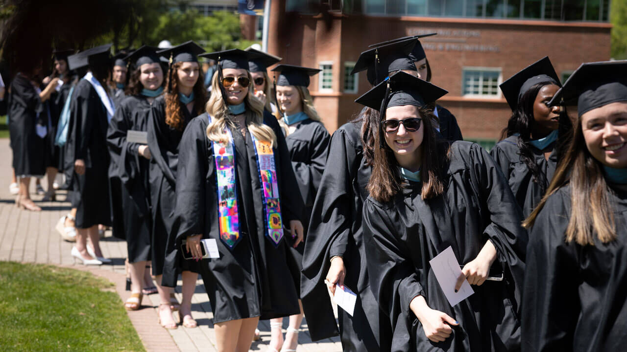 Dozens of graduates walk along a brick path on the quad
