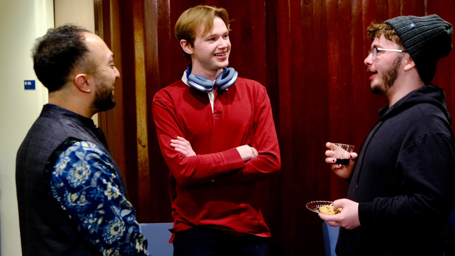 Three people, including a Butter Chicken band member, smiling and talking during a post-concert reception at Quinnipiac.