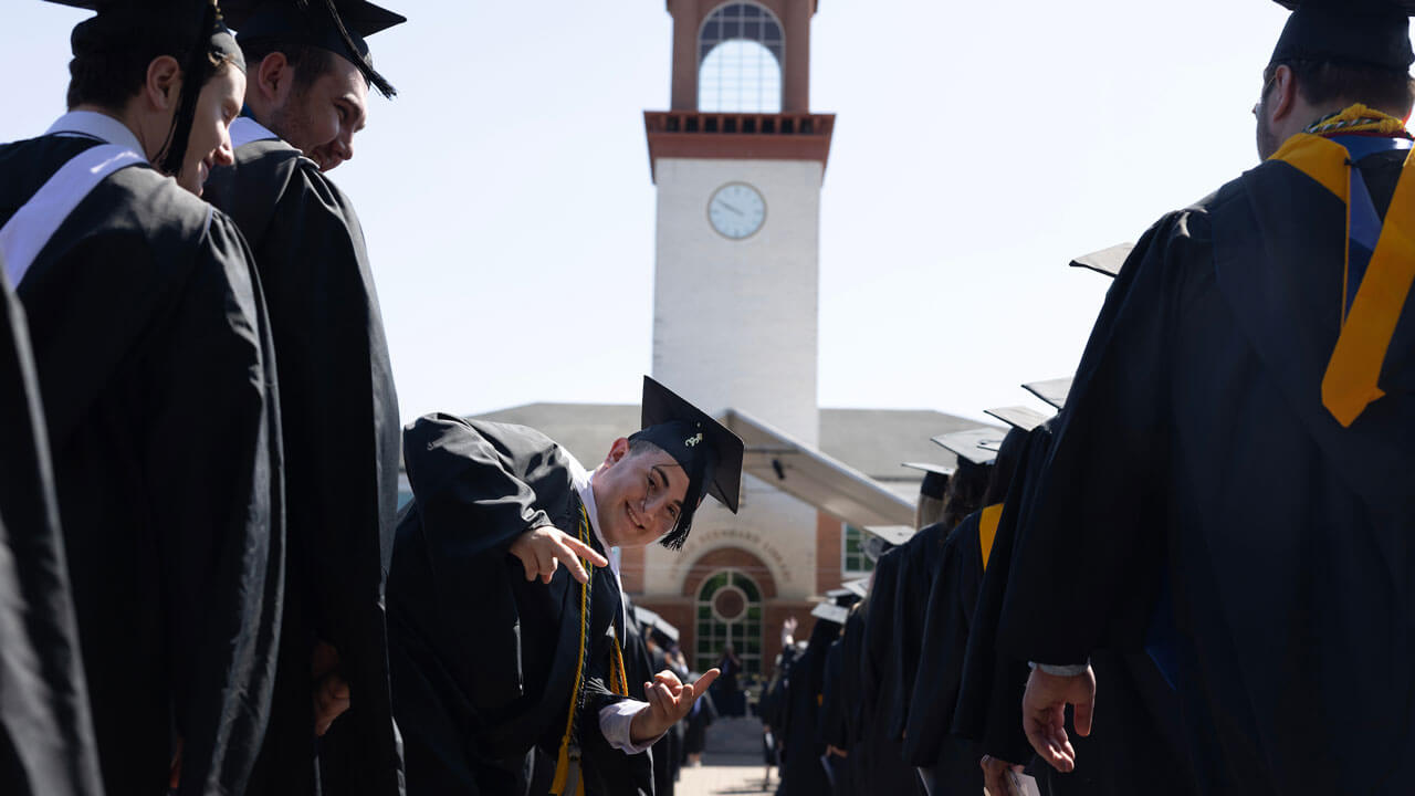 Graduate signals peace sign looking at camera while in line