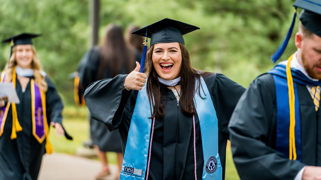 A graduate does a thumbs up and smiles