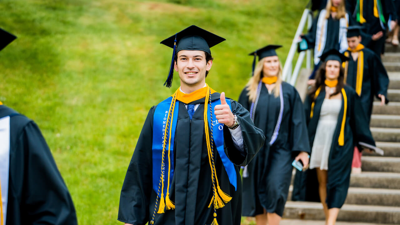 A graduate walks down the stairs and gives a thumbs up