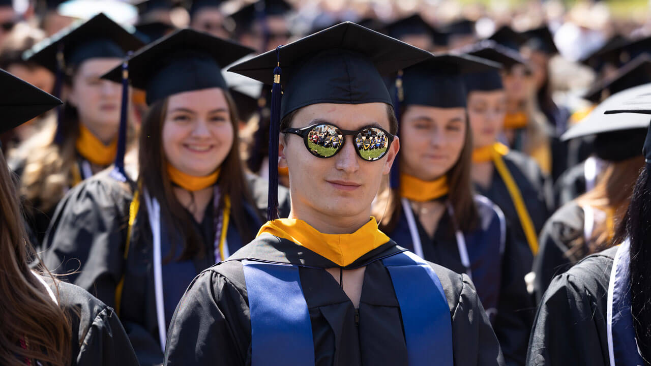 Rows of graduates reflect in a graduate's sunglasses as he sits during the ceremony