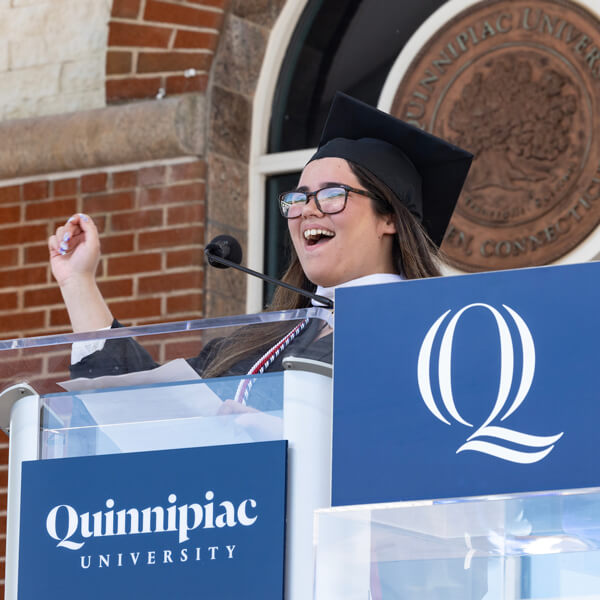Jamie Manley cheers with her hand in the air while she stands behind the Quinnipiac podium