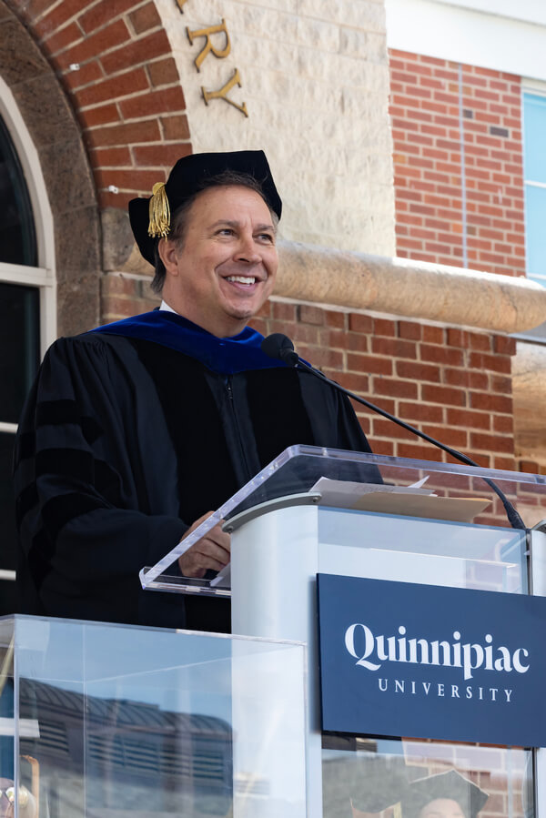 Dennis House wears commencement robes and speaks at the Quinnipiac lecturn