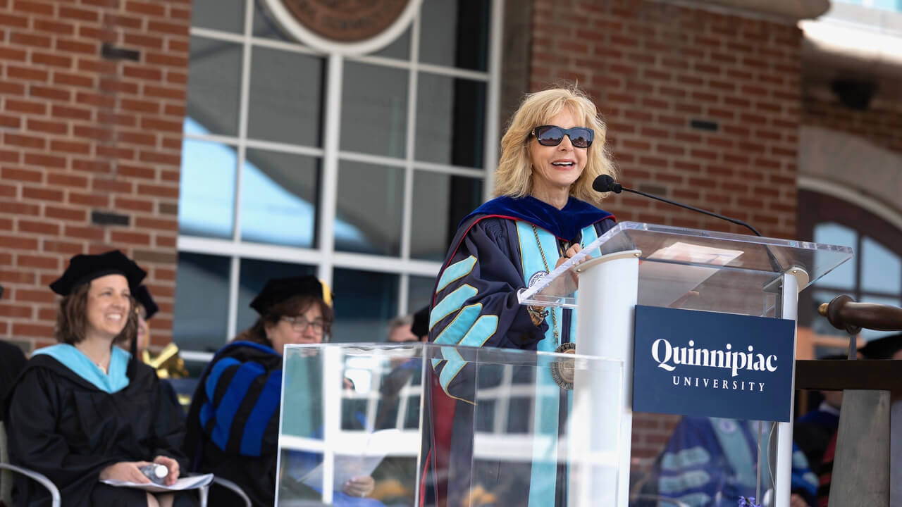 President Olian smiles broadly as she speaks at a Quinnipiac podium