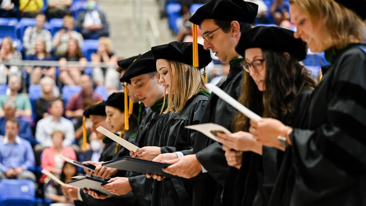 Dozens of medical students in commencement robes recite the Hippocratic Oath together