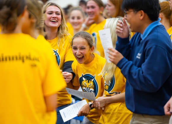 A new student in a gold Bobcats shirt doubles over with laughter surrounded by new students