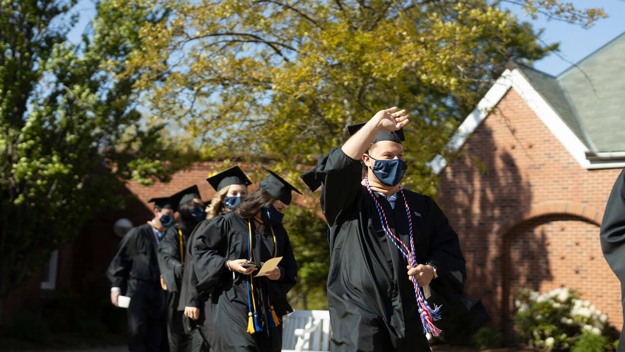 2020 graduate waving while walking into commencement ceremony