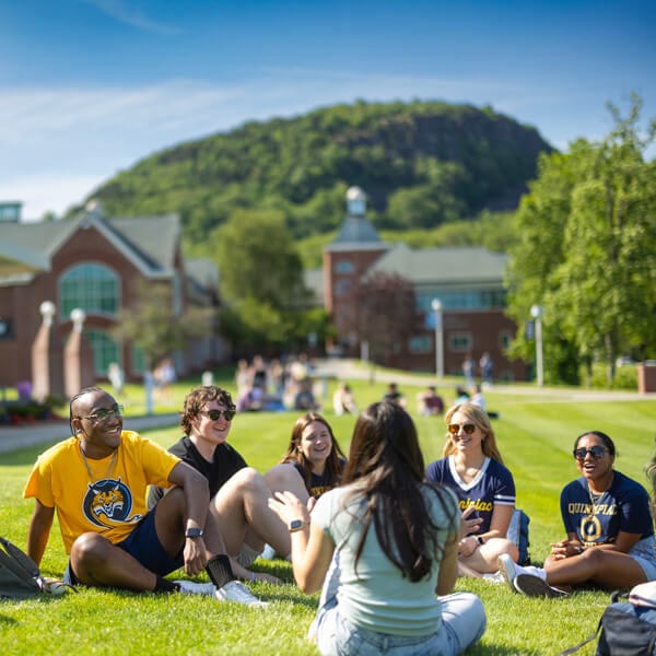 A group of students sit and talk on the Quad grass with the Sleeping Giant in the background