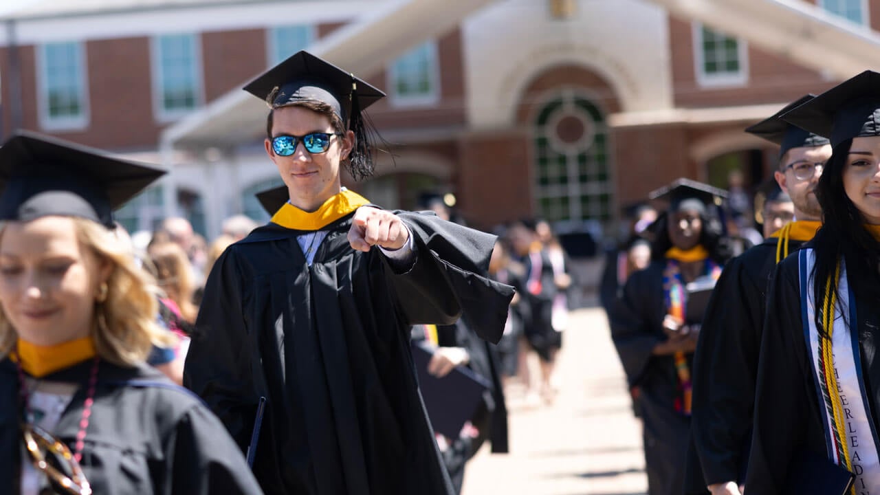 Graduate points proudly walking alongside other graduates happily
