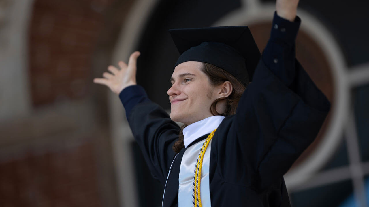Graduate throws arms in the air while grinning