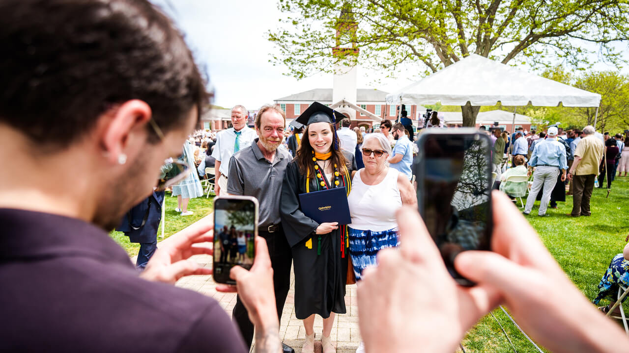 Two people take photos of a graduate on the quad