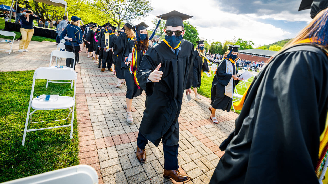 Graduate giving thumbs up to camera while walking into commencement ceremony