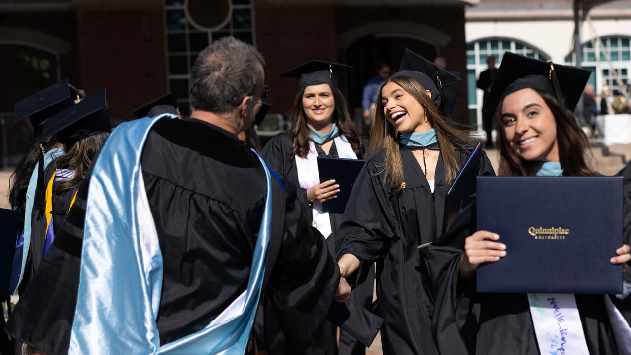 Three graduates shake hands and smile with a professor