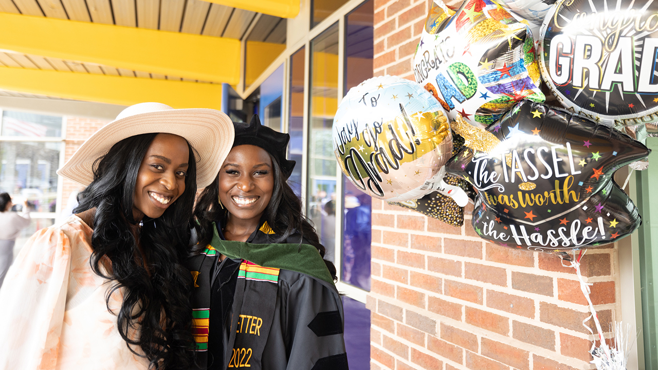 A graduate smiles with a relative and balloons
