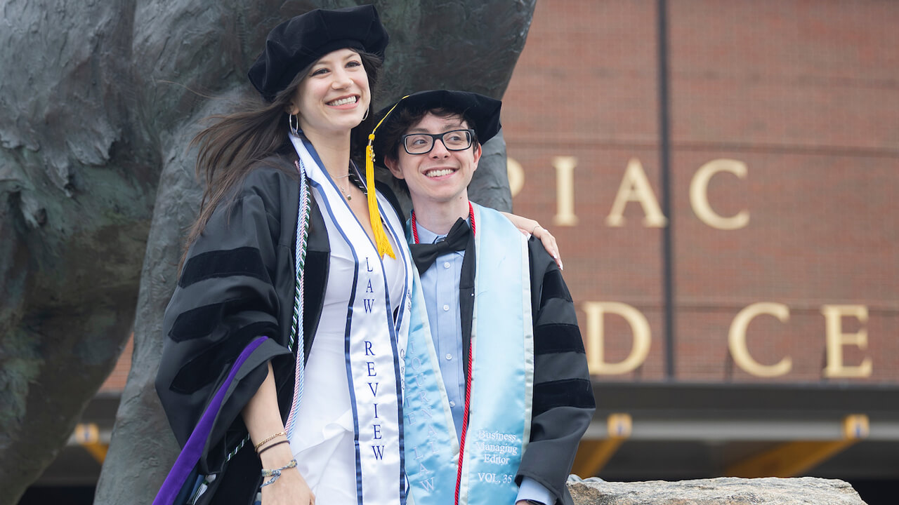 Two graduates smile in front of the bobcat statue