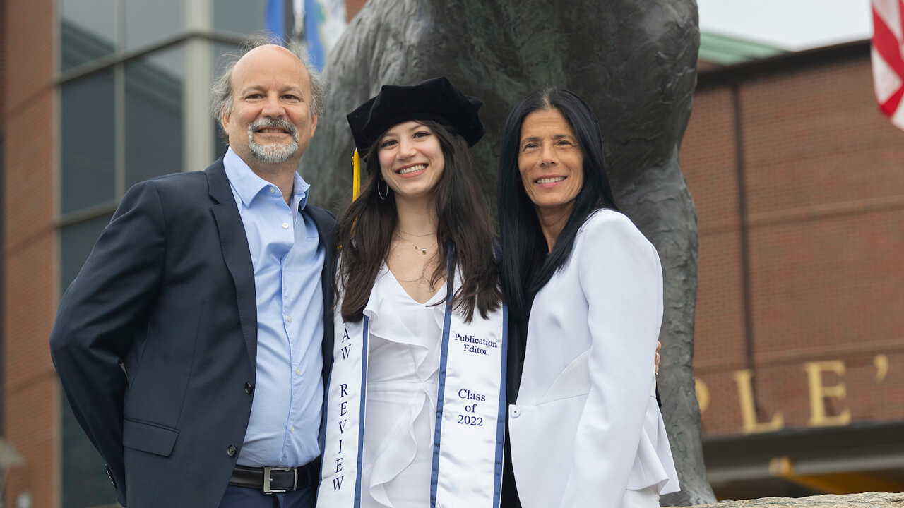 A graduate stands with relatives in front of the bobcat statue