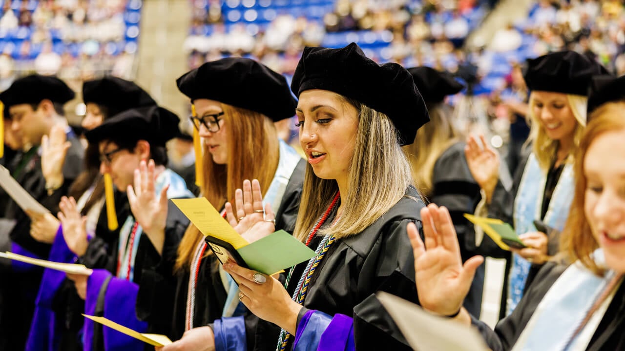 Law graduates hold up their right hand and recite an oath from papers in their hands