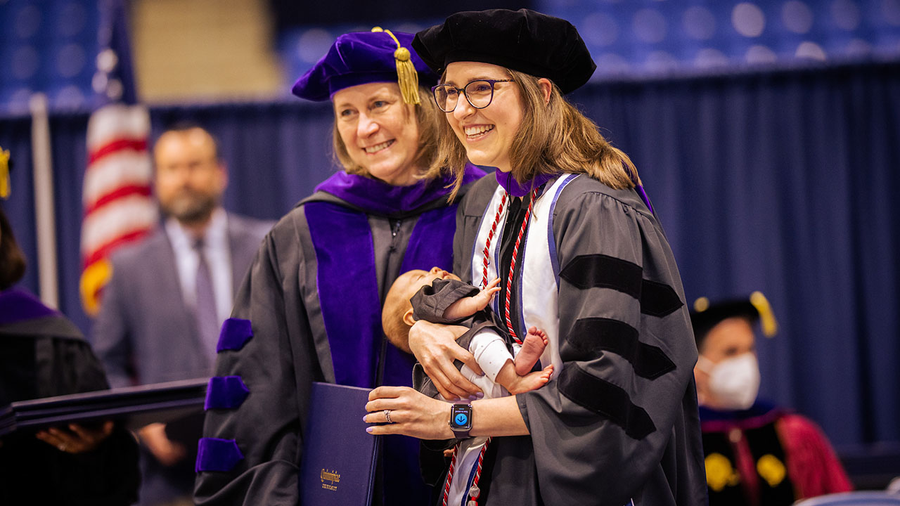 A graduate hold theirs infant as they get their diploma on stage