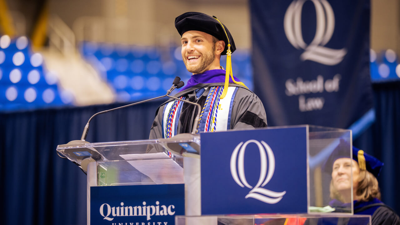 Kyle Souza smiles broadly as he speaks at the Quinnipiac Commencement podium