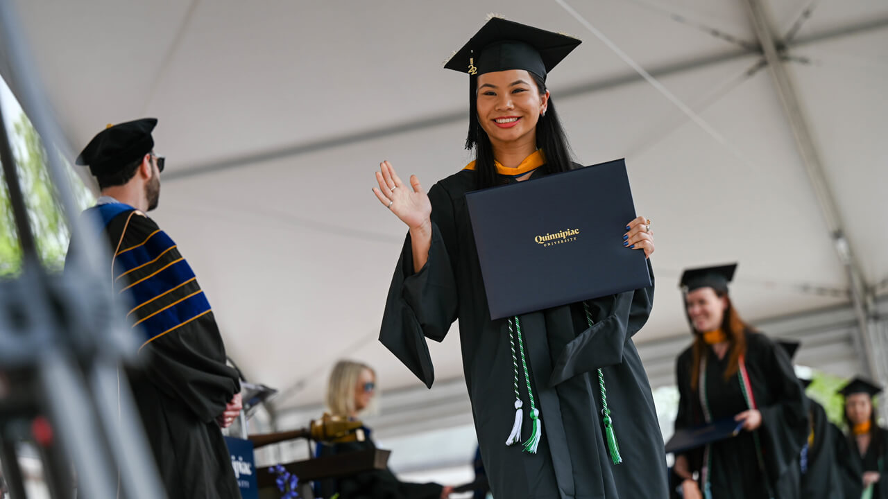 Graduate smiles and waves as she holds her diploma