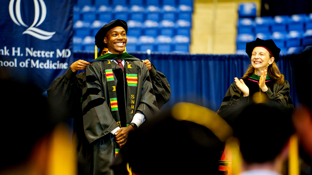 A graduate smiles while being hooded at the school of medicine commencement